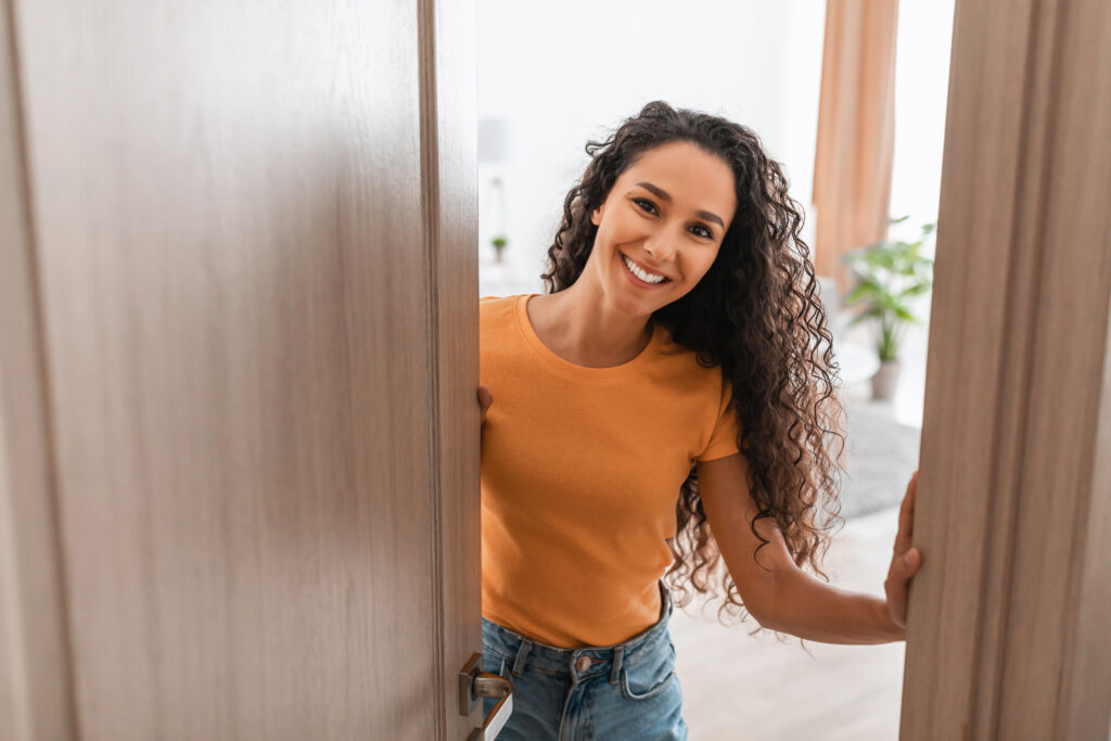 cheerful-young-curly-lady-receiving-guests-at-fron-2022-12-16-07-07-44-utc